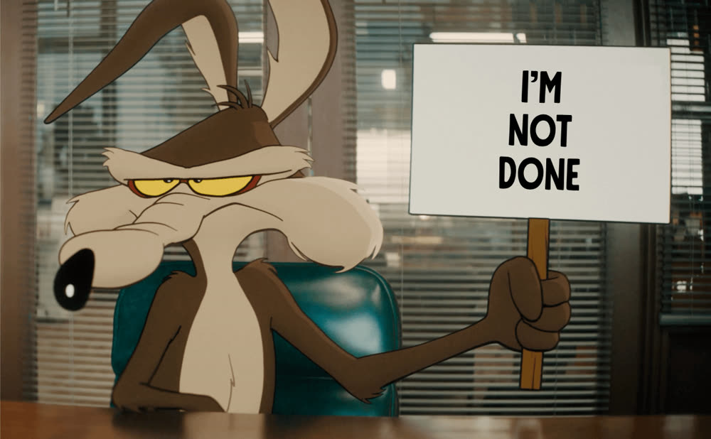 Wile E. Coyote sits at an office desk and holds up a
                      sign that reads I'm not done.